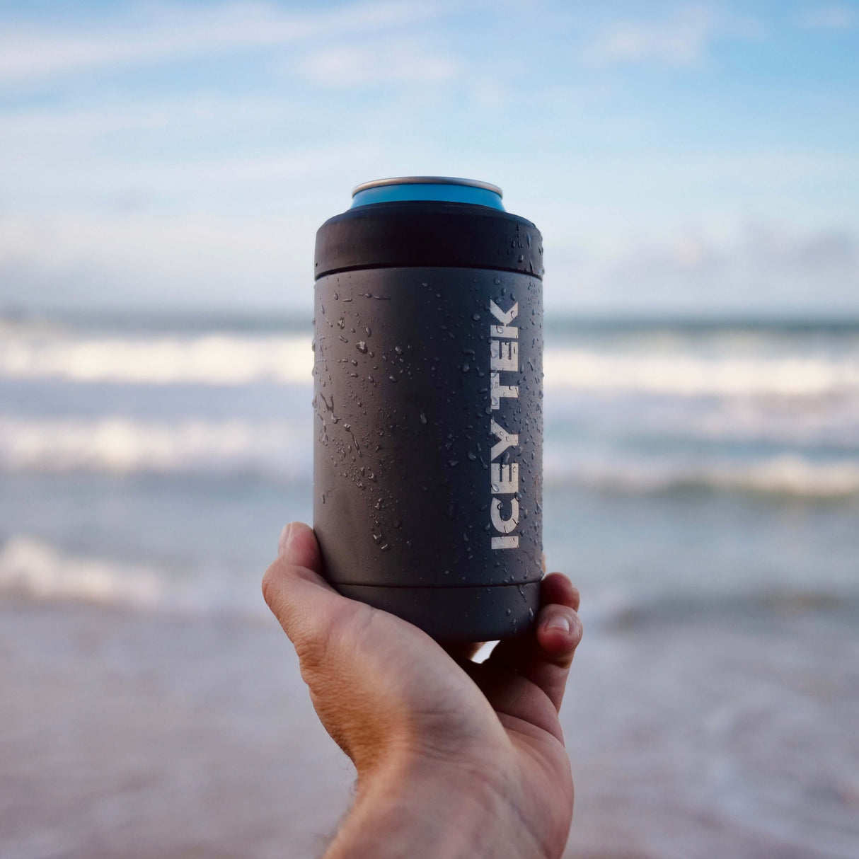 Hand holding an ICETEK insulated cup on a beach with ocean in the background