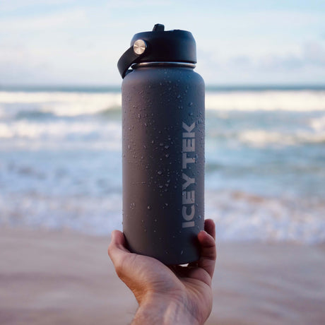 Hand holding an ICY TEK water bottle with a beach background