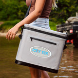Person holding an Icey Tek cooler by a body of water with a truck in the background.